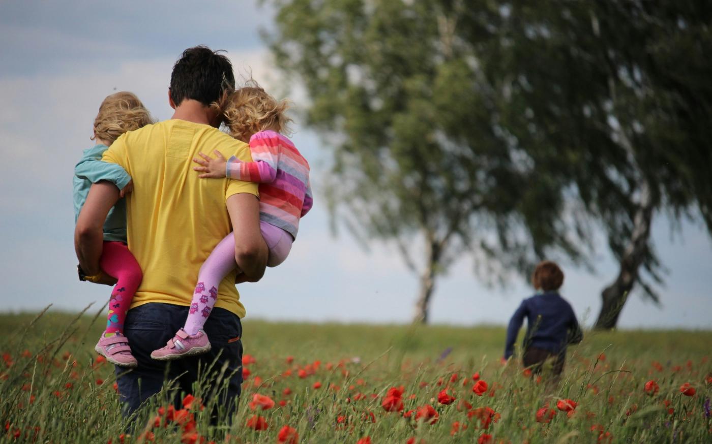 man carrying to girls on field of red petaled flower by Juliane Liebermann courtesy of Unsplash.